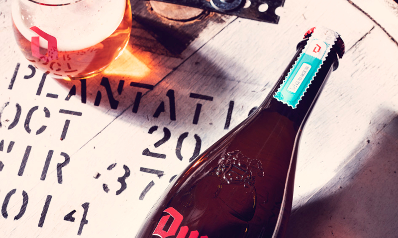 Duvel Barrel Aged Batch 5 The Rum Edition glas op een vat met de fles er liggend naast